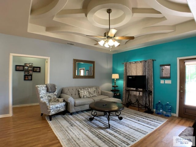 living room featuring a raised ceiling, ceiling fan, and hardwood / wood-style flooring