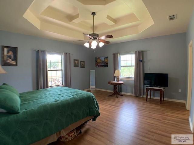 bedroom with hardwood / wood-style flooring, ceiling fan, a raised ceiling, and multiple windows