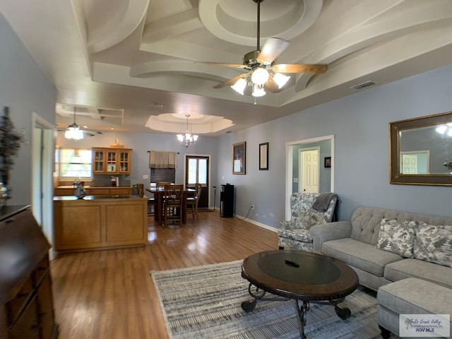 living room with ceiling fan with notable chandelier, light hardwood / wood-style floors, and a tray ceiling