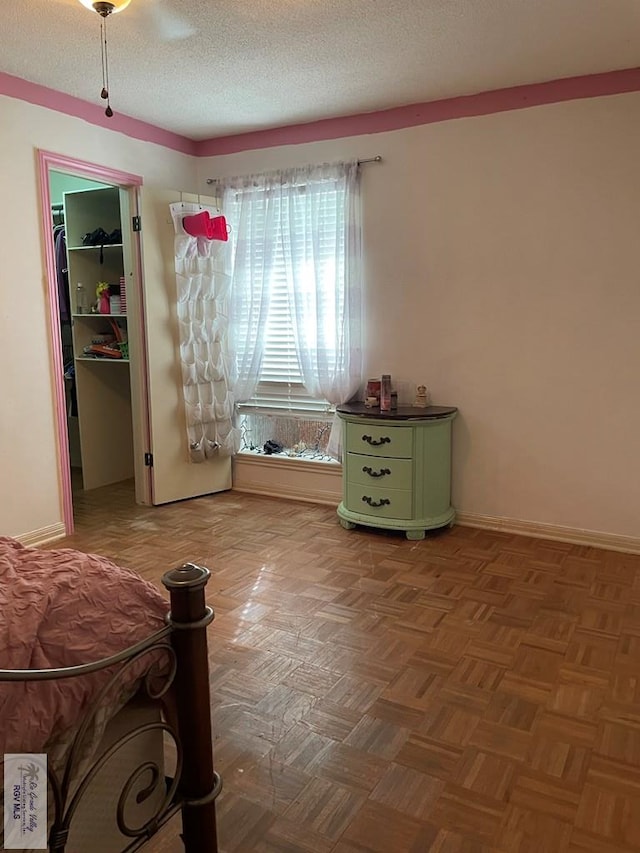 bedroom featuring a walk in closet, a textured ceiling, parquet floors, and ceiling fan