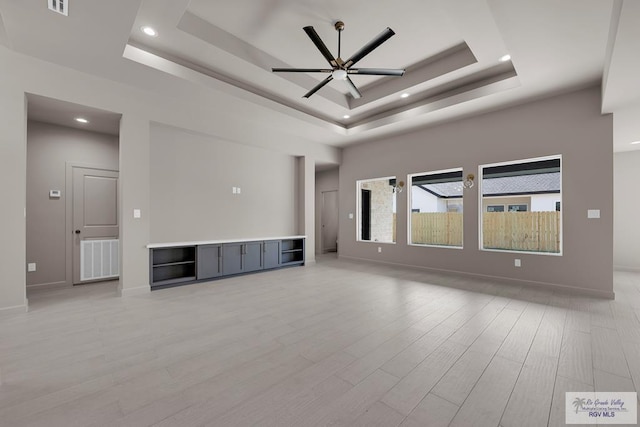 unfurnished living room with visible vents, ceiling fan, baseboards, light wood-type flooring, and a tray ceiling