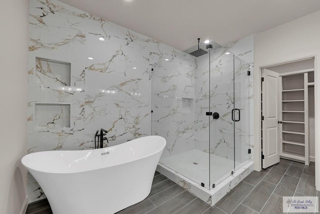 bathroom featuring a marble finish shower, stone wall, a walk in closet, and a freestanding tub