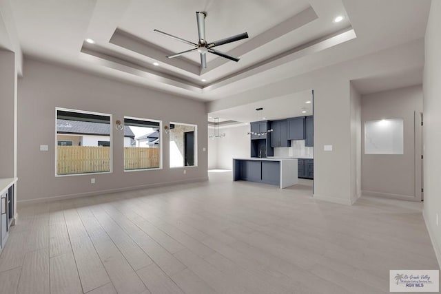 unfurnished living room featuring baseboards, light wood finished floors, a tray ceiling, recessed lighting, and ceiling fan