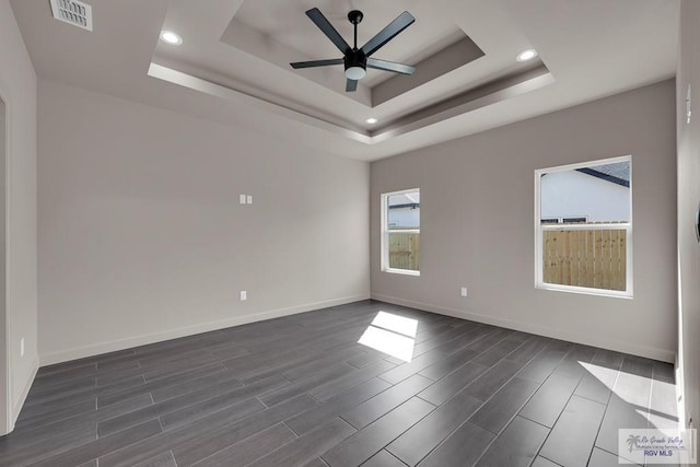 unfurnished room featuring a raised ceiling, a ceiling fan, visible vents, and wood finish floors