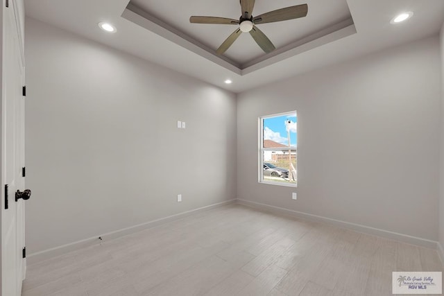 unfurnished room featuring ceiling fan, baseboards, light wood-style flooring, and a tray ceiling