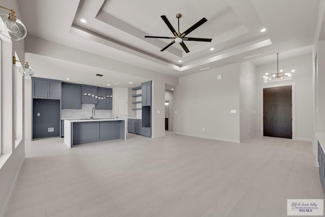 unfurnished living room with baseboards, a raised ceiling, light wood-style floors, and ceiling fan with notable chandelier