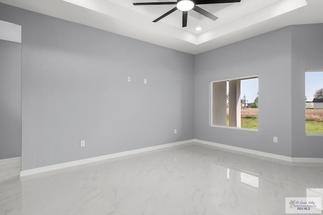 spare room featuring a wealth of natural light, a tray ceiling, marble finish floor, and baseboards