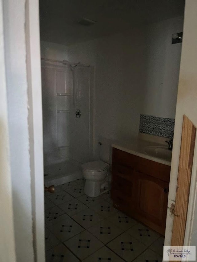 bathroom with tiled shower, vanity, toilet, and tile patterned flooring