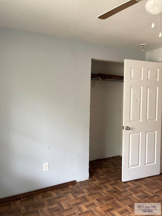 unfurnished bedroom featuring ceiling fan, a closet, and dark parquet floors