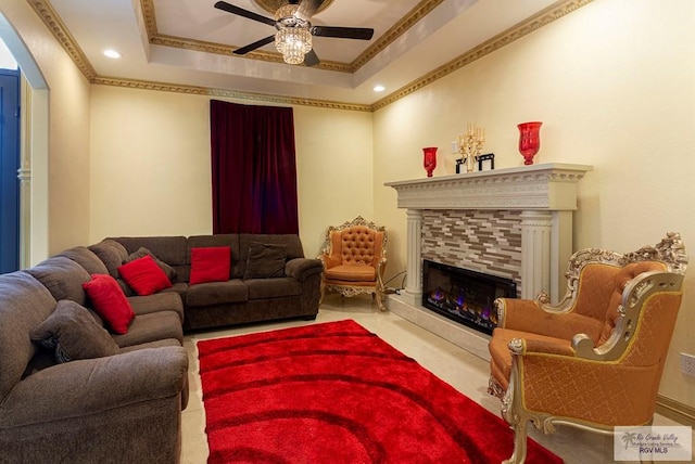 living room with ceiling fan, ornamental molding, a tray ceiling, and a tiled fireplace