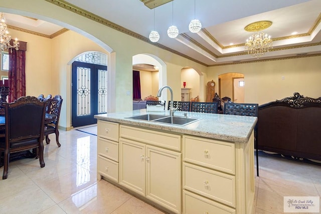 kitchen with light stone counters, sink, a center island with sink, a notable chandelier, and hanging light fixtures