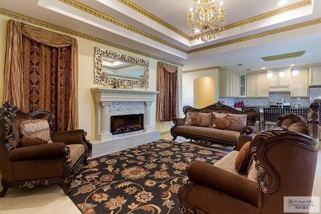 living room featuring a notable chandelier, a raised ceiling, ornamental molding, and a fireplace