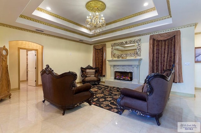 living room featuring a high end fireplace, a raised ceiling, a notable chandelier, and crown molding