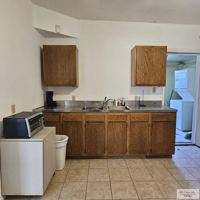 kitchen with a toaster, stacked washer and dryer, a sink, brown cabinetry, and dark countertops