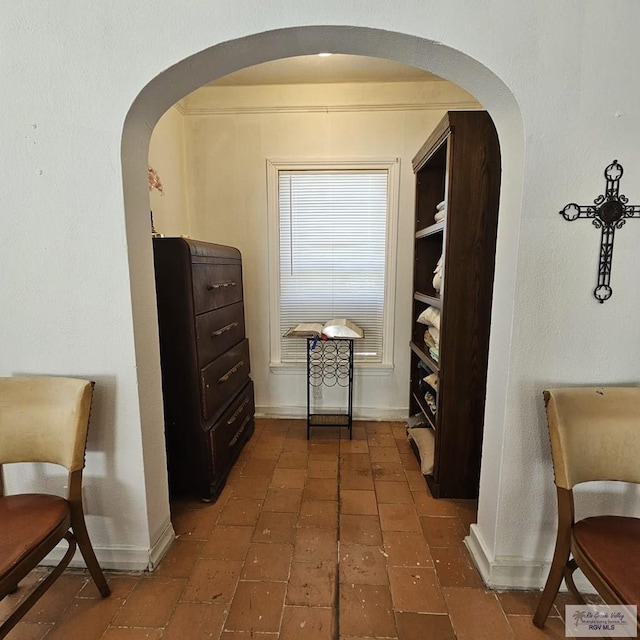 corridor featuring arched walkways, brick floor, and baseboards