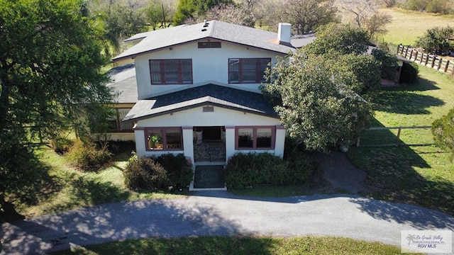 view of front of property featuring fence, a chimney, a front lawn, and stucco siding