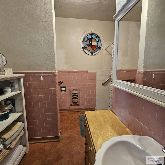 bathroom with a wainscoted wall, tile walls, a textured wall, a sink, and a textured ceiling