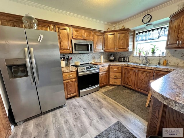 kitchen with appliances with stainless steel finishes, backsplash, crown molding, sink, and light hardwood / wood-style floors