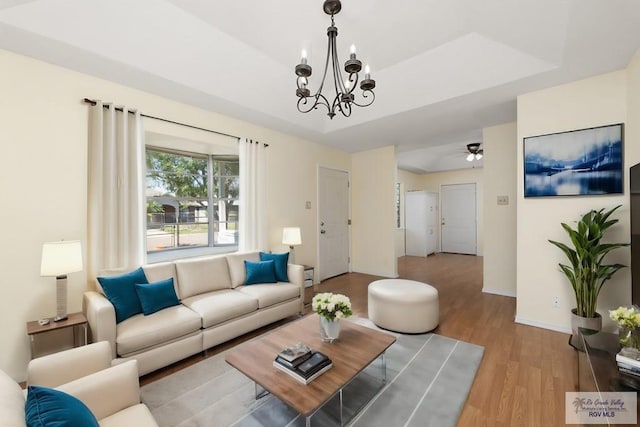 living room featuring ceiling fan with notable chandelier, a tray ceiling, and light hardwood / wood-style flooring