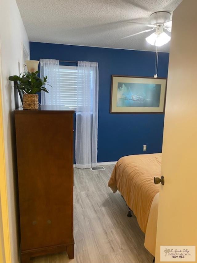 bedroom with a textured ceiling, light hardwood / wood-style flooring, and ceiling fan