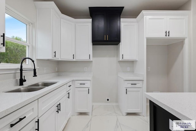 kitchen with light stone countertops, sink, and white cabinets