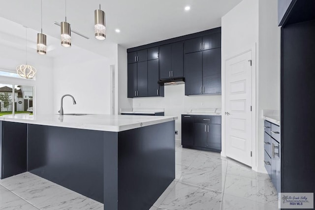 7332 San Andres St, Brownsville, TX 78520 - kitchen featuring a sink, dark cabinetry, under cabinet range hood, hanging light fixtures, and light marble finish flooring