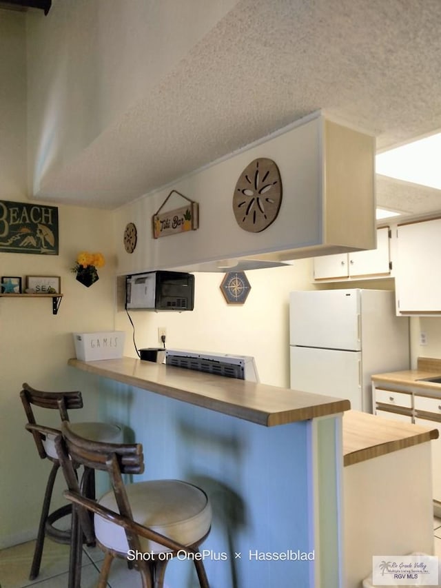 kitchen featuring a kitchen bar, a peninsula, white cabinets, and freestanding refrigerator