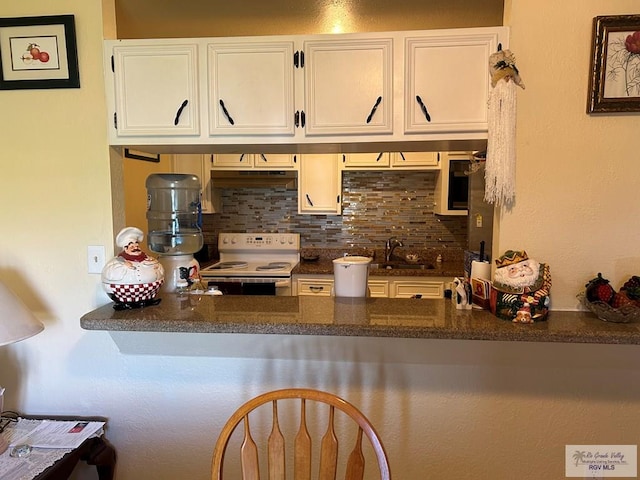 kitchen with white cabinetry, electric range, sink, tasteful backsplash, and dark stone countertops