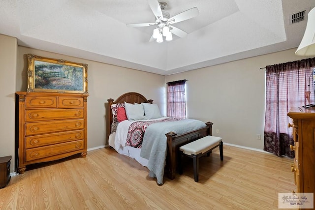 bedroom with light hardwood / wood-style flooring, a raised ceiling, and ceiling fan