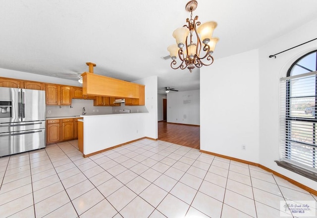 kitchen featuring light tile patterned floors, a peninsula, stainless steel fridge with ice dispenser, a sink, and light countertops