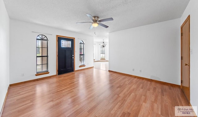 foyer entrance featuring baseboards, ceiling fan with notable chandelier, a textured ceiling, and light wood finished floors