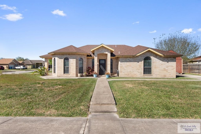 view of front of home with brick siding, a front lawn, and fence