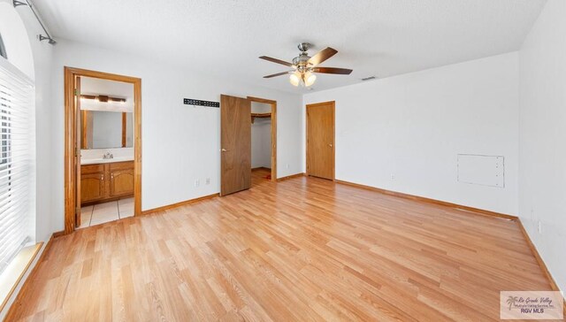 unfurnished bedroom featuring baseboards, visible vents, a sink, light wood-style floors, and connected bathroom