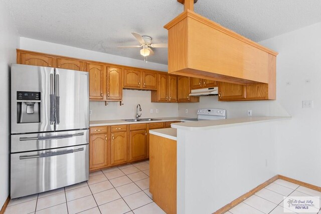 kitchen with under cabinet range hood, light countertops, range, stainless steel refrigerator with ice dispenser, and a sink