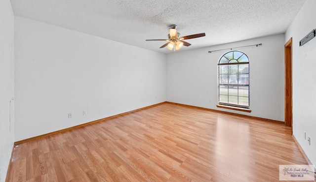 spare room featuring ceiling fan, light wood-style floors, baseboards, and a textured ceiling