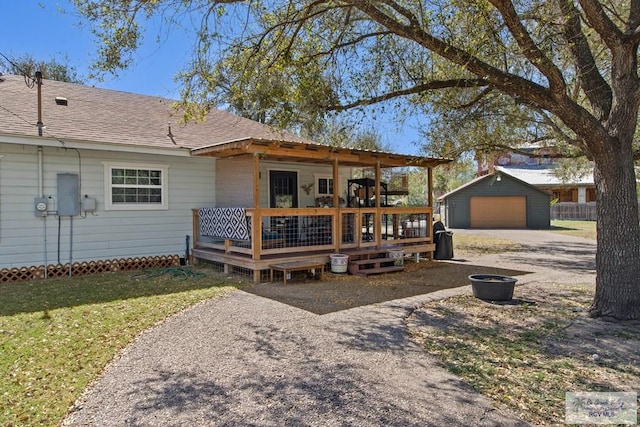 view of front facade with a shingled roof, a detached garage, a front lawn, an outdoor structure, and driveway