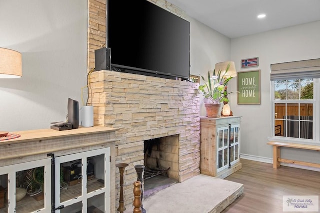 living area featuring a stone fireplace, recessed lighting, baseboards, and wood finished floors