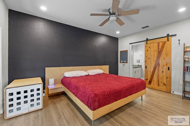 bedroom featuring recessed lighting, a barn door, wood finished floors, and an accent wall