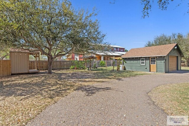 exterior space with driveway, a shingled roof, an outdoor structure, and fence