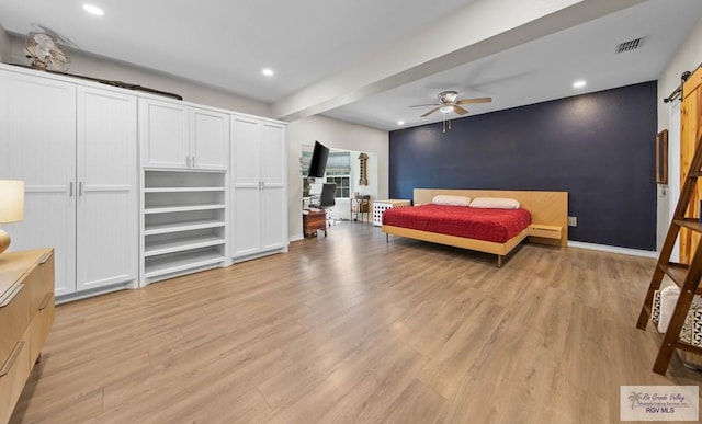 bedroom featuring light wood-type flooring, recessed lighting, a barn door, baseboards, and an accent wall