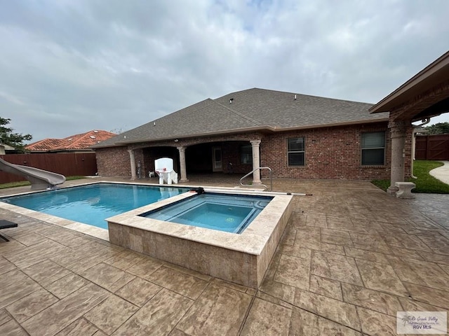 view of swimming pool with a water slide, a patio, and an in ground hot tub