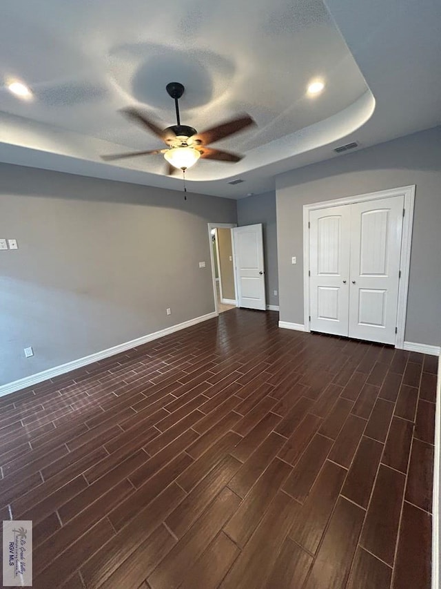 interior space with dark wood-type flooring, ceiling fan, and a tray ceiling