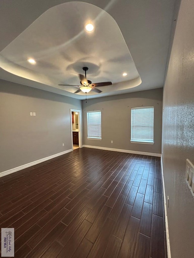 empty room with dark hardwood / wood-style floors, a wealth of natural light, ceiling fan, and a tray ceiling