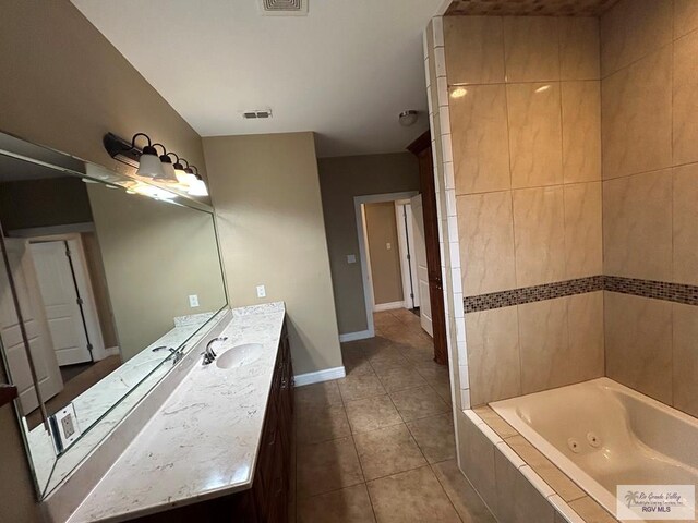 bathroom with a relaxing tiled tub, vanity, and tile patterned flooring