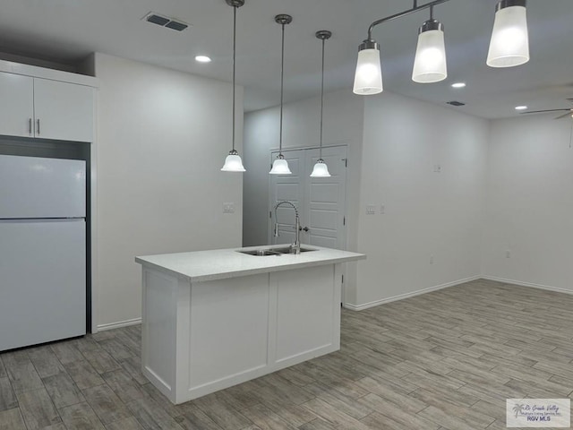 kitchen featuring white cabinetry, sink, hanging light fixtures, white fridge, and an island with sink