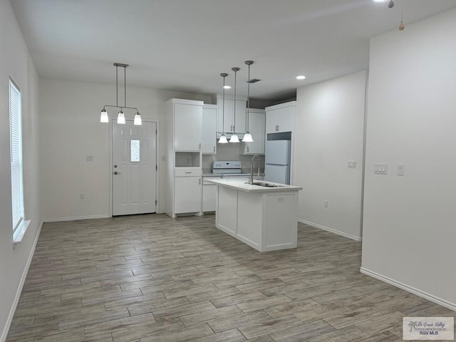 kitchen with white appliances, decorative light fixtures, a center island with sink, light hardwood / wood-style flooring, and white cabinetry