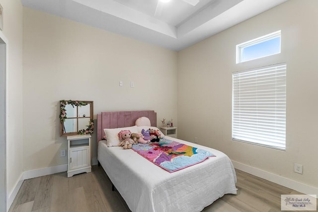 bedroom featuring ceiling fan, light hardwood / wood-style floors, and a raised ceiling