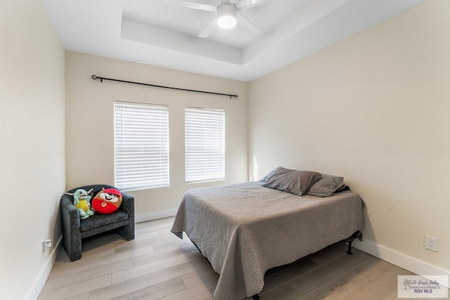 bedroom with ceiling fan, light hardwood / wood-style floors, and a tray ceiling