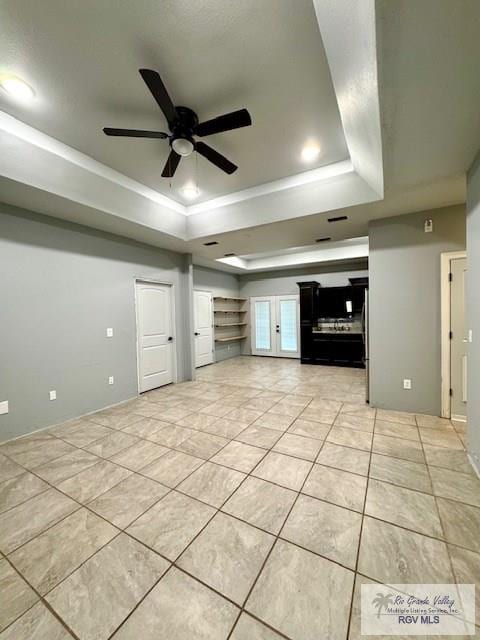 unfurnished living room with a tray ceiling, ceiling fan, and light tile patterned flooring