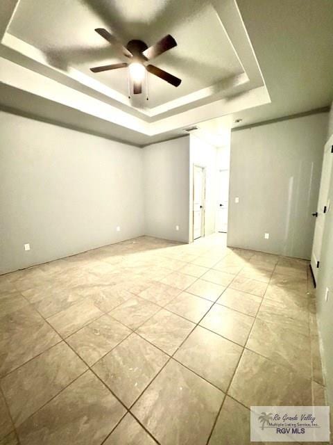 unfurnished room with ceiling fan and a tray ceiling